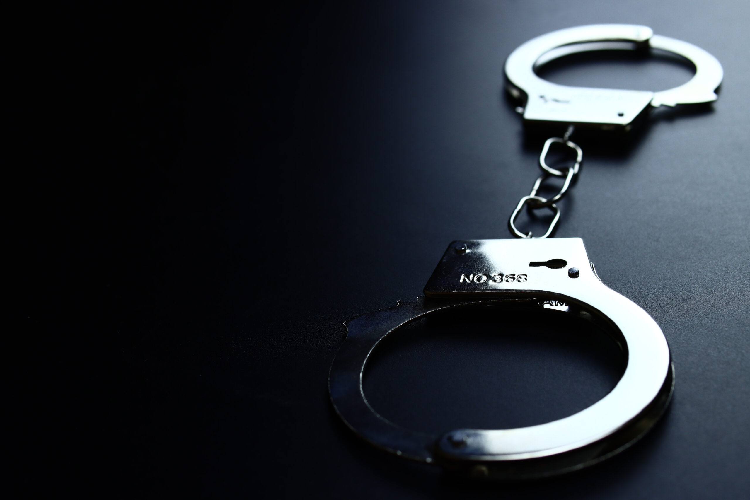 Police metal handcuffs on black background, close-up, selective focus