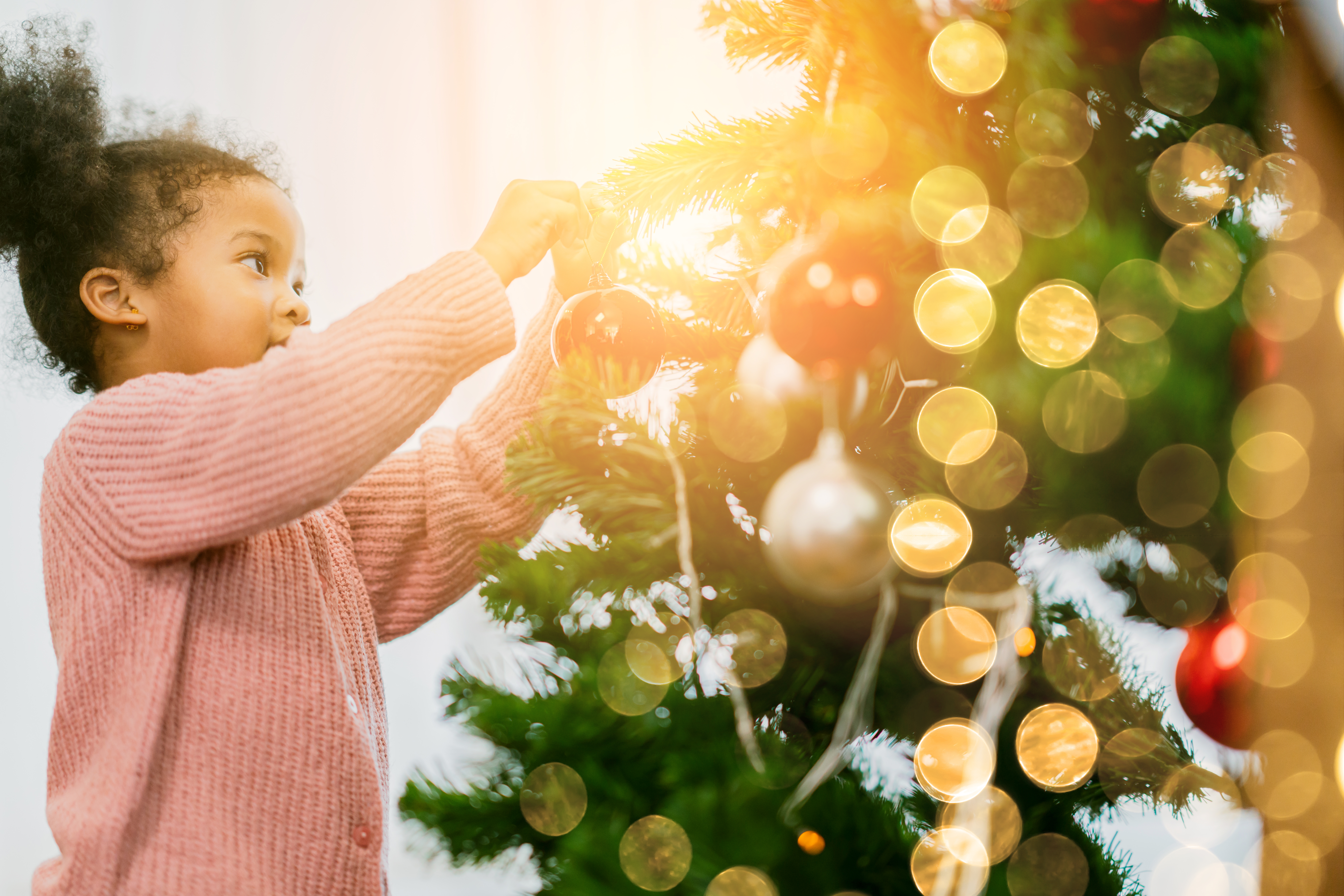 child hanging ornaments on tree holidays