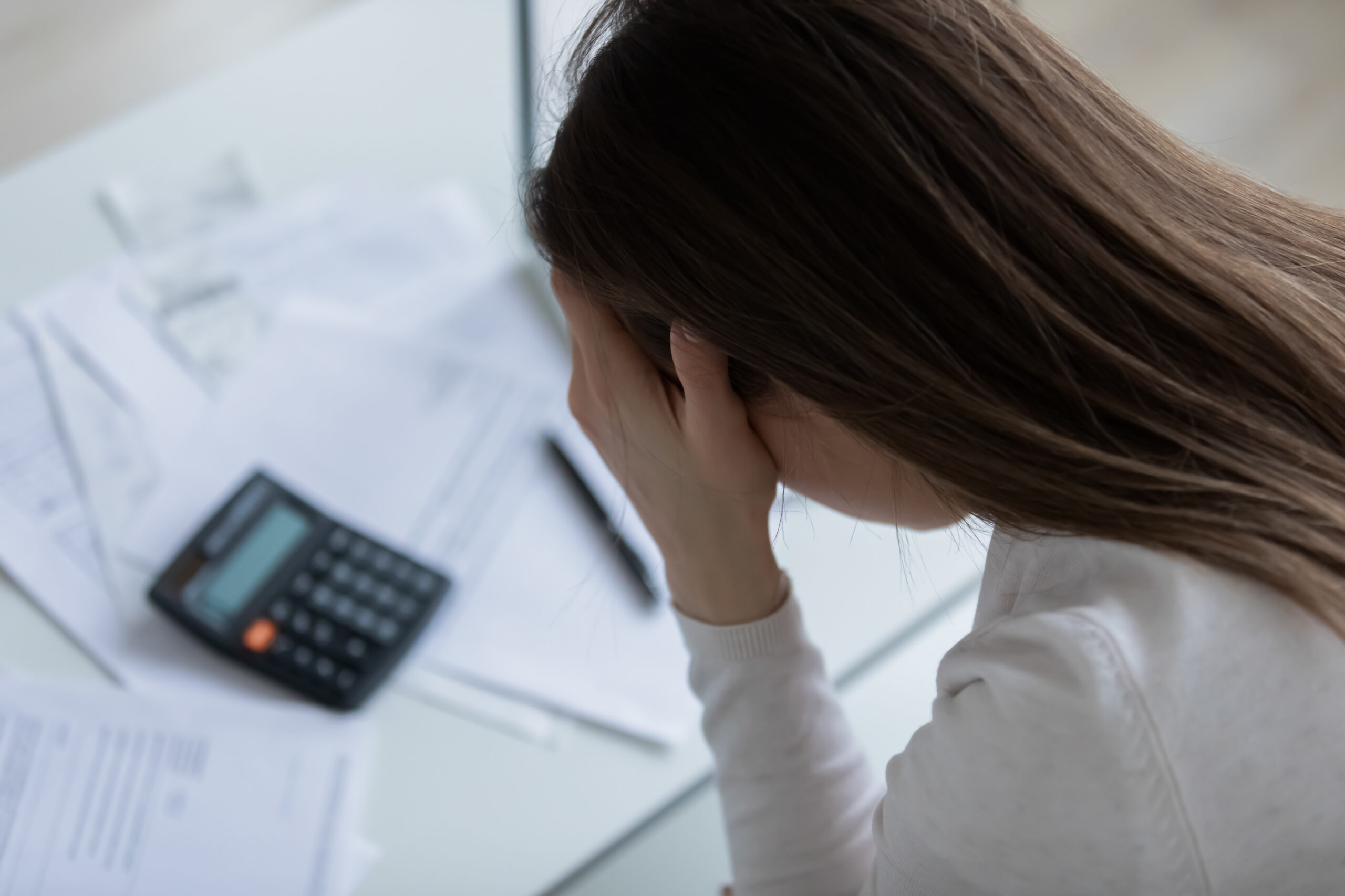 Close up above top view woman holds her head with hands feels desperate after calculating expenses having financial problems, lack of money pay bills domestic household utilities, high taxes concept