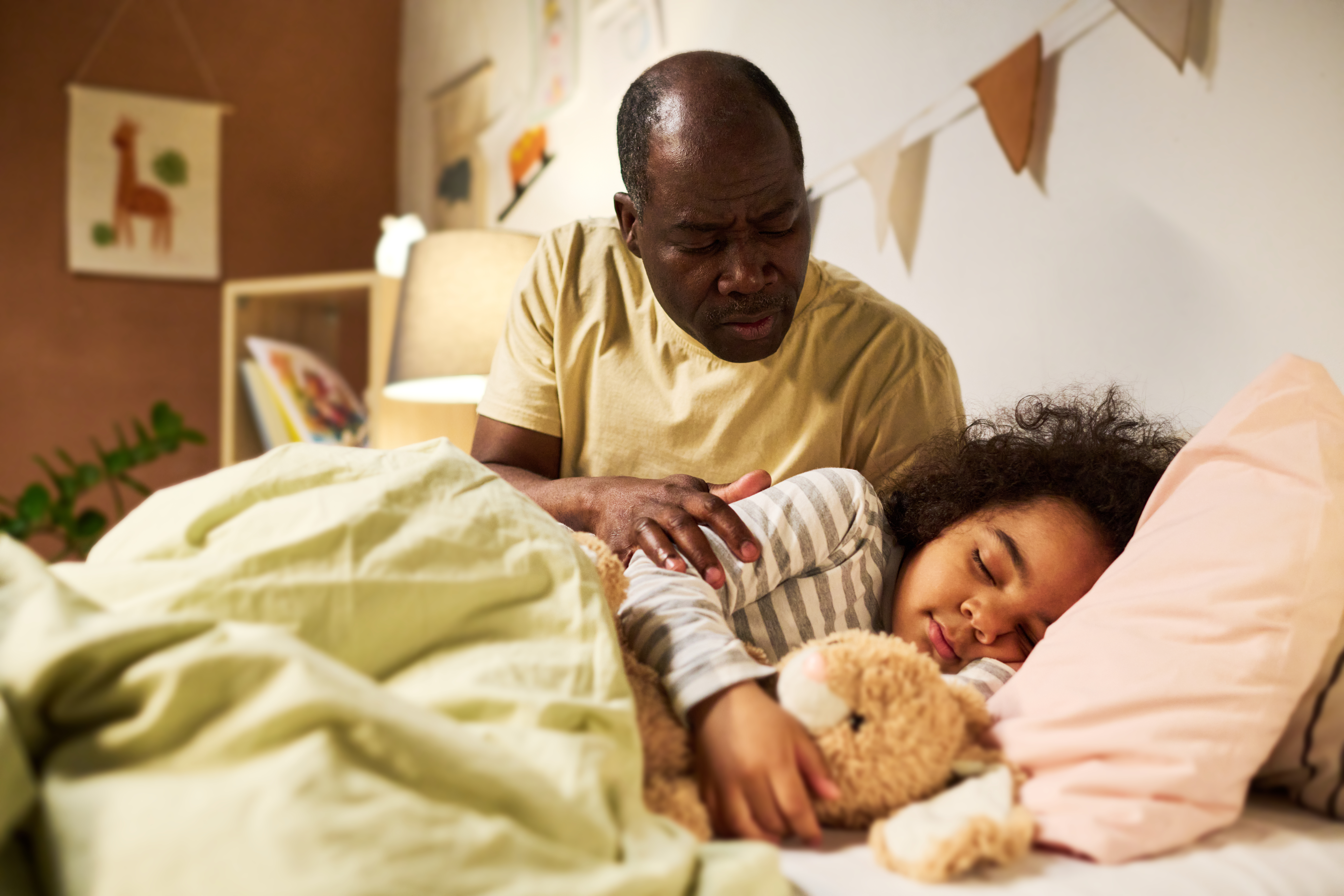 Little son sleeping in his bed with toy while dad putting him and telling tale to him